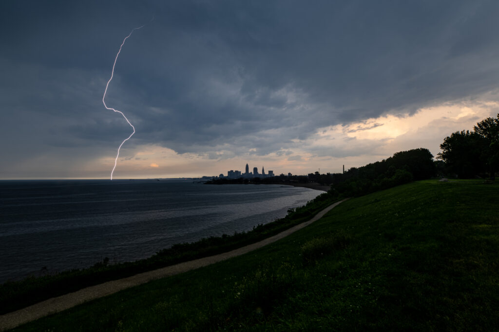 Lightning strikes over coastal city skyline at twilight with winding shore road wallpaper background