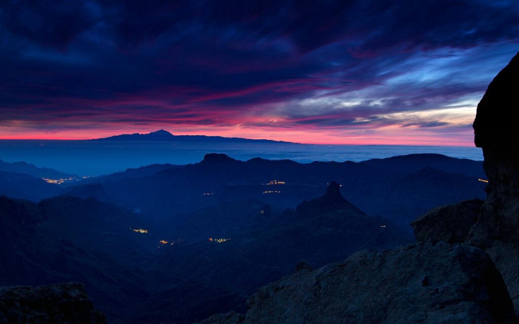 Dramatic twilight mountain wallpaper with deep blue purple sky red pink streaks and distant lights