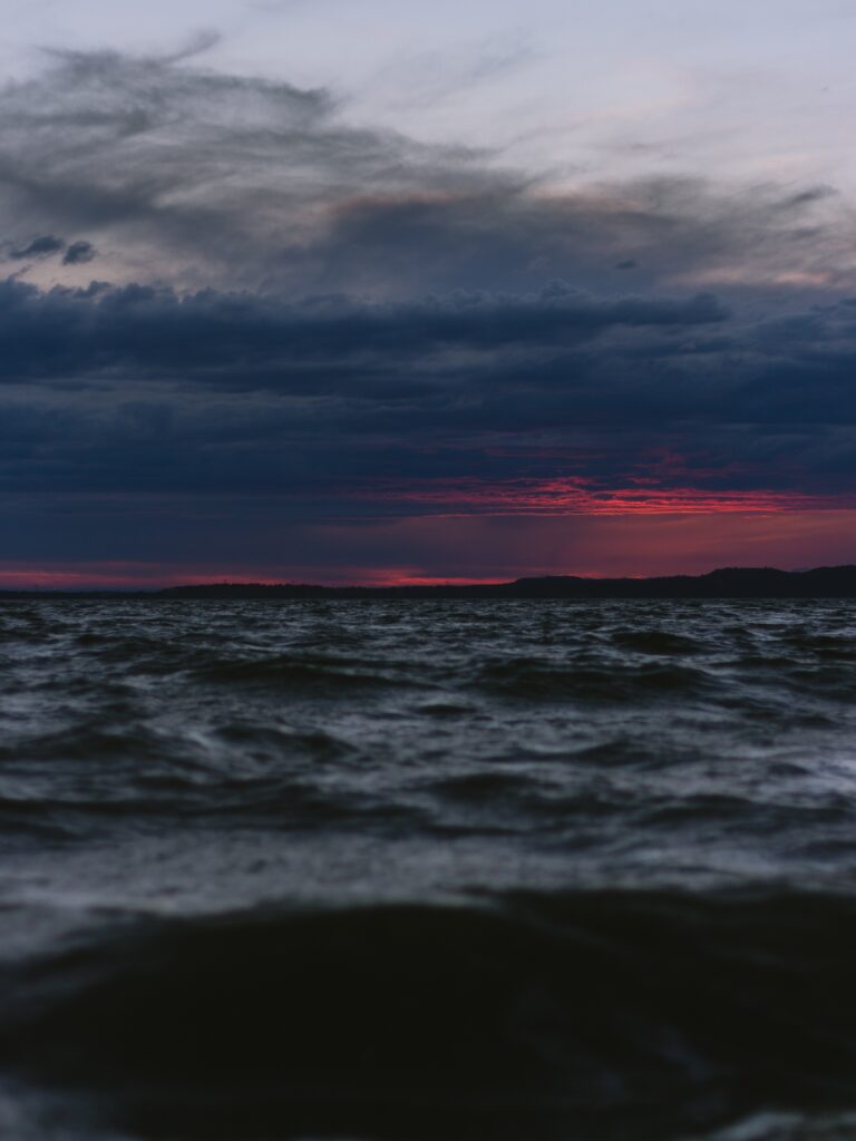 Dramatic twilight seascape with dark waves and vibrant red purple sunset on moody cloudy sky Wallpaper