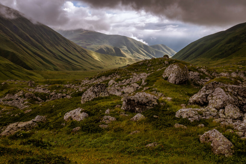 Dramatic valley with rolling green hills rocky terrain wild grass and moody cloudy sky wallpaper