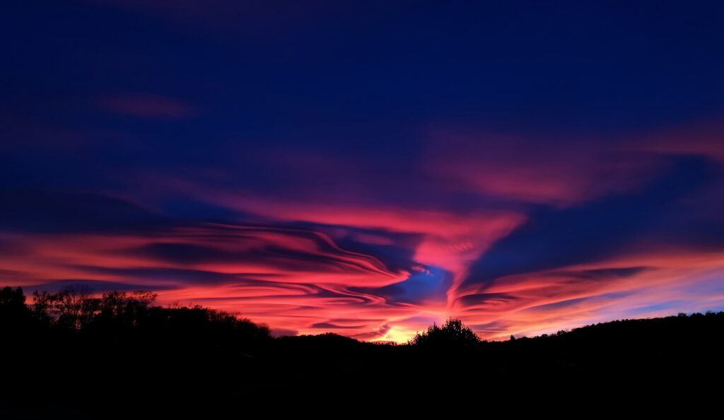 Vivid sunset clouds swirling in fiery orange and deep purple above a dark landscape background Wallpaper