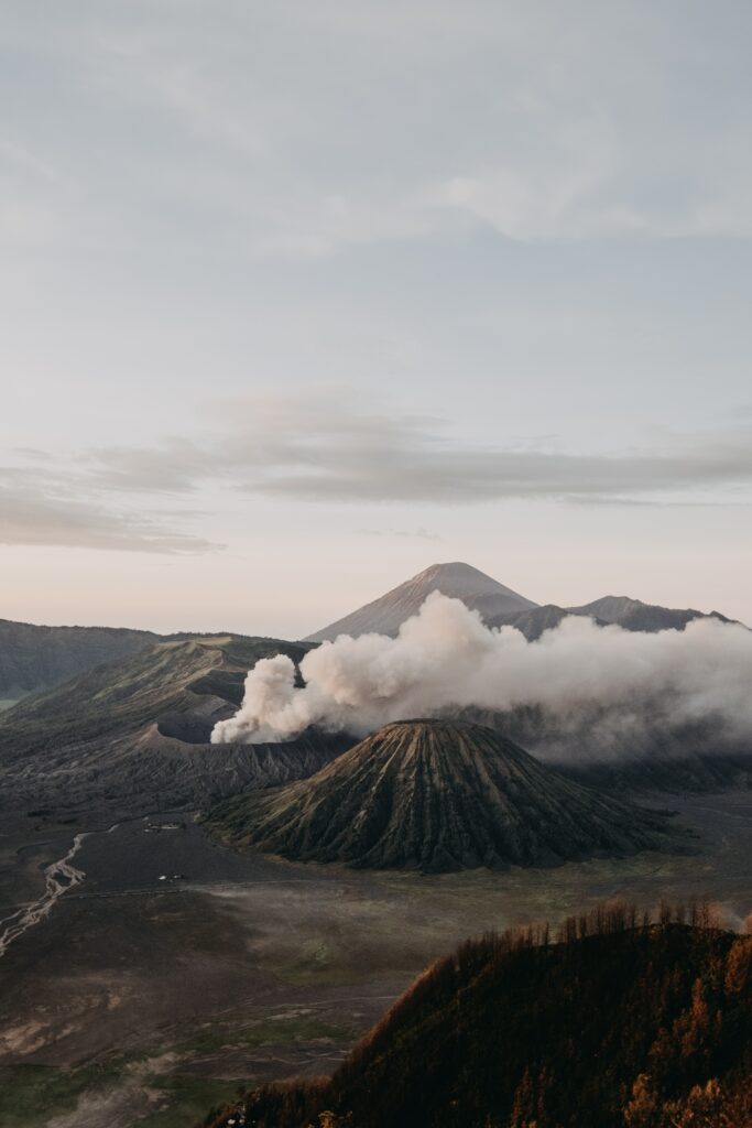 Volcanic landscape with erupting craters smoke rugged terrain under pastel sky wallpaper background