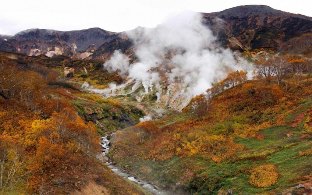 Volcanic landscape wallpaper with steam smoke rugged mountains and vibrant autumn foliage background