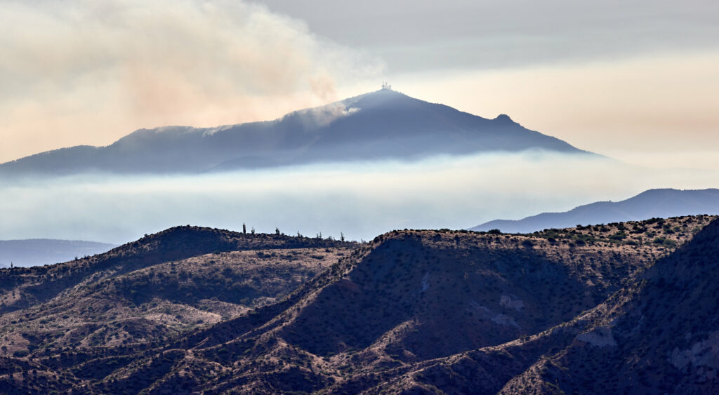 Volcanic mountain peak with drifting smoke and layered earthy hills under hazy sky wallpaper
