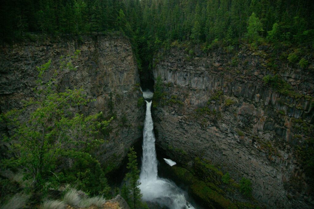 Dramatic waterfall flowing between rugged cliffs into canyon surrounded by lush green forest Wallpaper