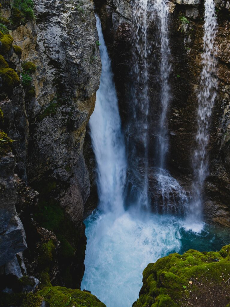 Dramatic waterfall cascading over rugged cliff with mossy rocks into turquoise pool wallpaper