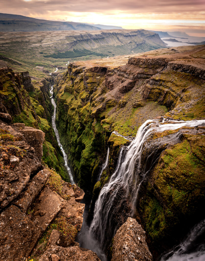 Dramatic waterfall cascading through rocky gorge with lush greenery and colorful sky wallpaper