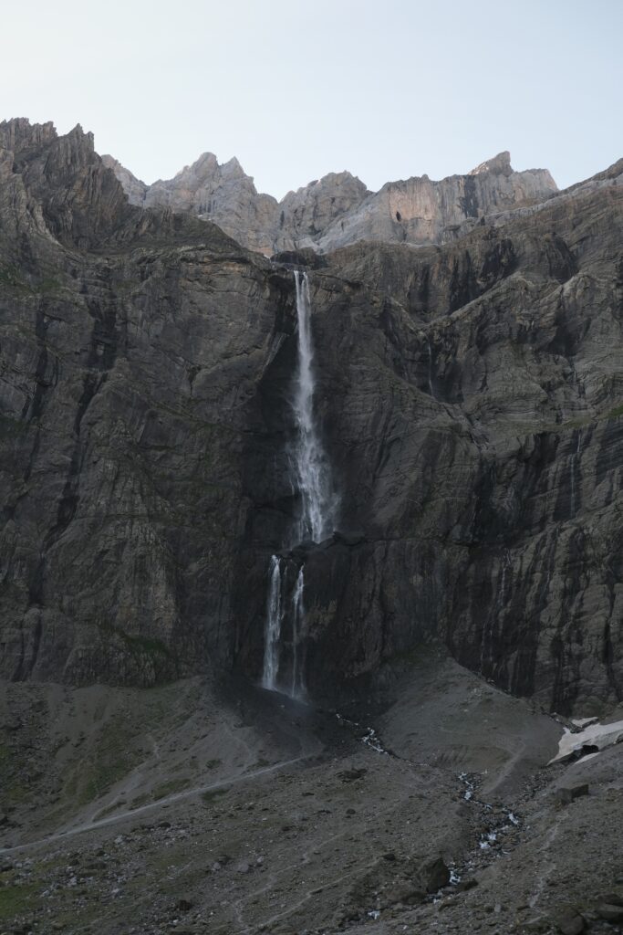 Dramatic waterfall cascading down rugged mountain cliffs with rocky terrain under pale sky wallpaper