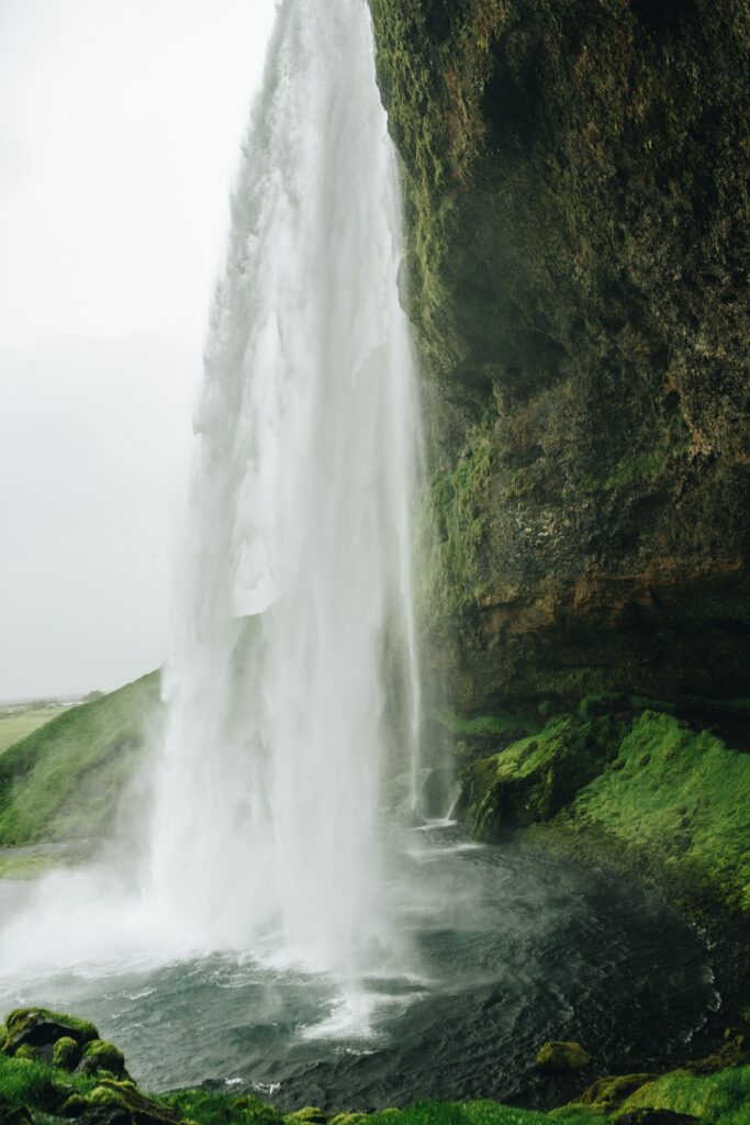 Powerful waterfall cascades dark cliff over green moss into swirling pool dramatic lush nature background Wallpaper