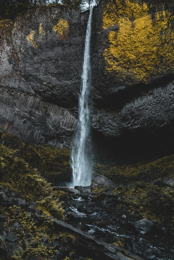 Dramatic waterfall cascading from cliff surrounded by mossy rocks lush greenery and layered stones Wallpaper