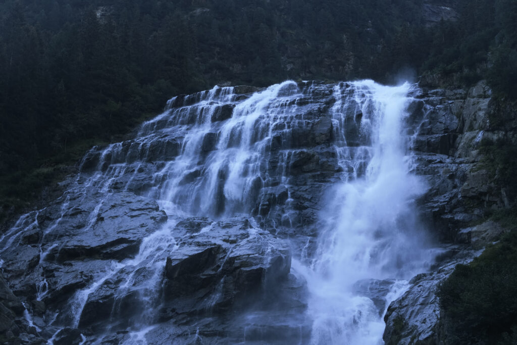 Dramatic waterfall cascading over rugged rocks surrounded by lush green forest and natural light Wallpaper