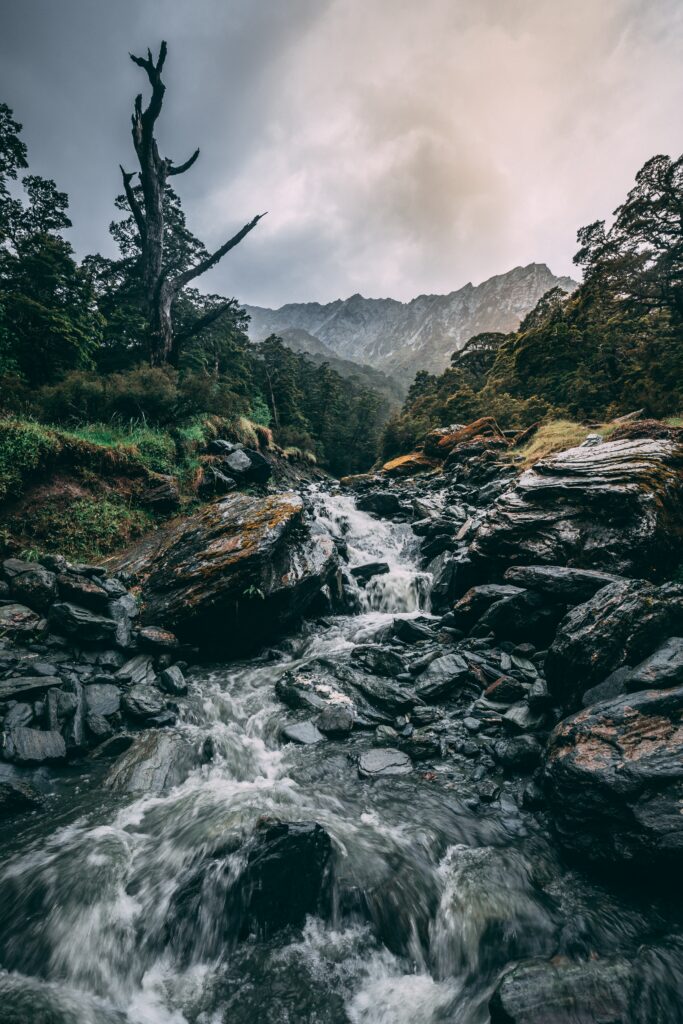 Dramatic waterfall over rugged stones with vibrant greenery and misty mountain background Wallpaper