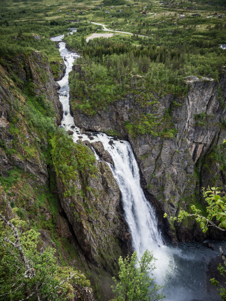 Dramatic waterfall cascading into gorge surrounded by towering rocks and lush green trees wallpaper