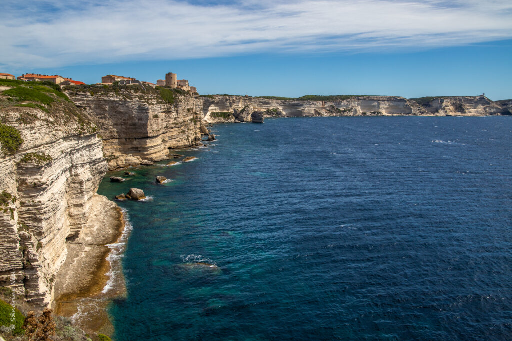 White limestone cliffs with coastal buildings above deep blue sea under partly cloudy sky wallpaper