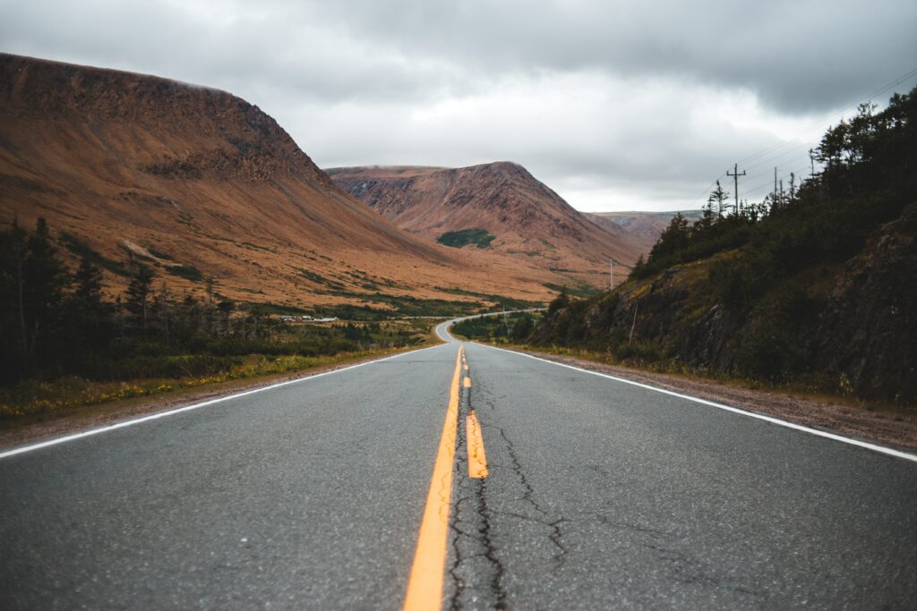 Winding road with yellow markings through rugged mountains under cloudy sky wallpaper background