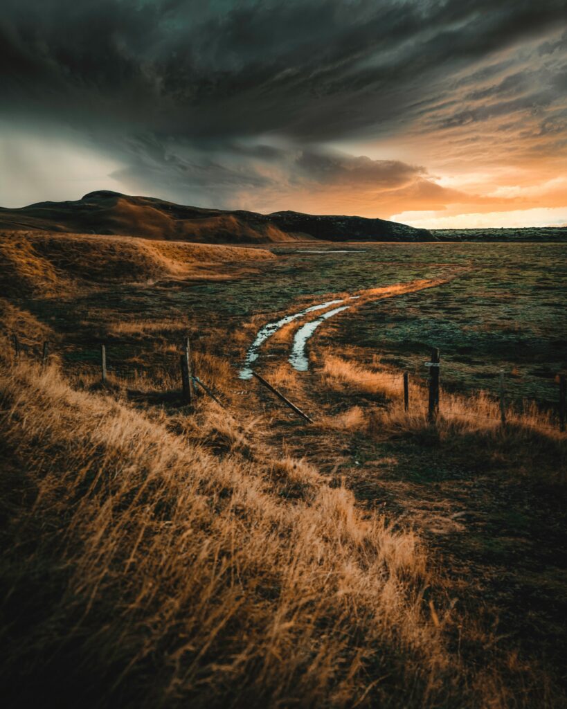 Winding road through golden fields and hills under dark stormy sky rural landscape wallpaper