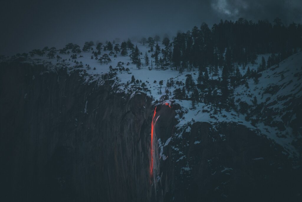 Lava flowing down snow-covered rocky cliff in foggy winter landscape vibrant contrast wallpaper