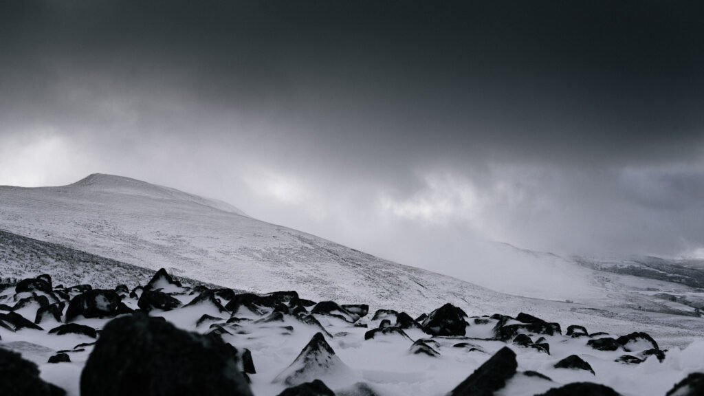 Snowy valley and hills with jagged rocks under a dark moody winter sky wallpaper background