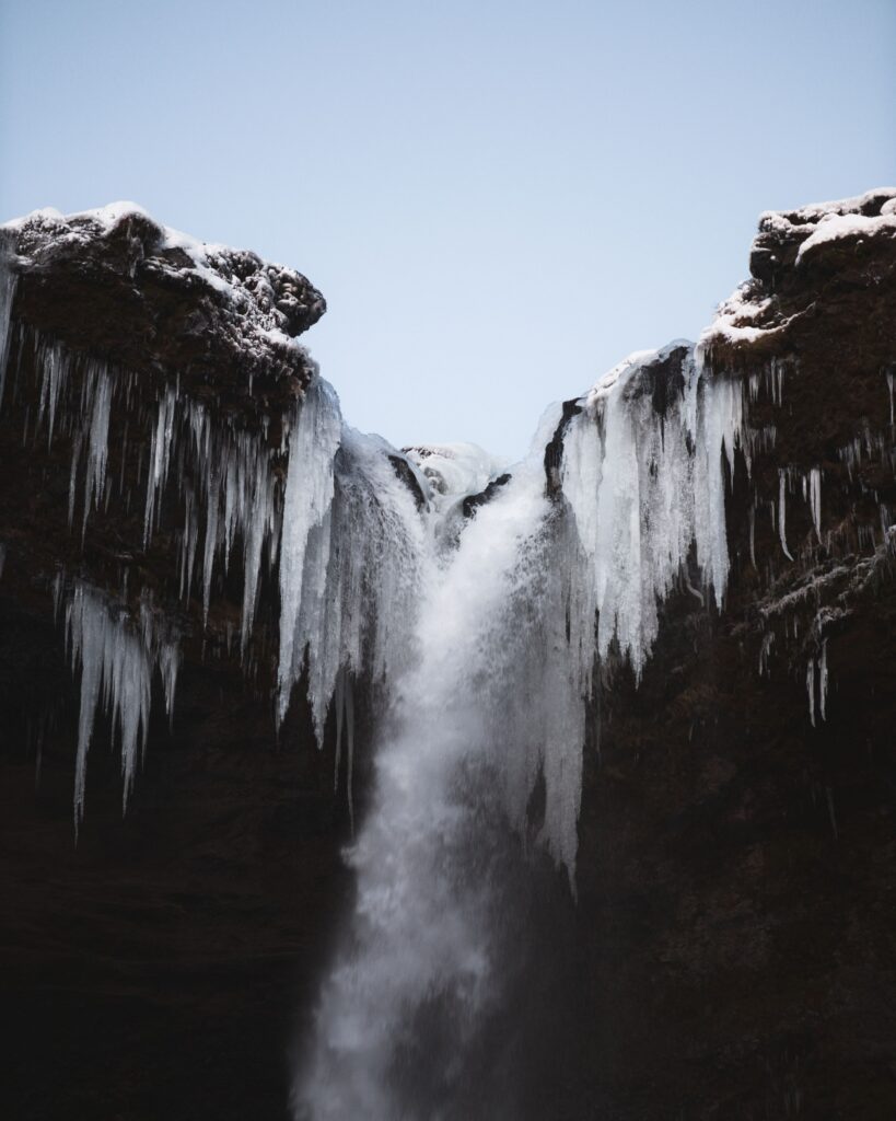 Winter waterfall cascading icy cliffs snow layers clear blue sky serene wallpaper background