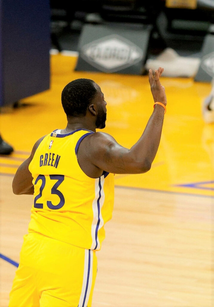 Draymond Green in vibrant yellow jersey playing intense basketball on polished court wallpaper background