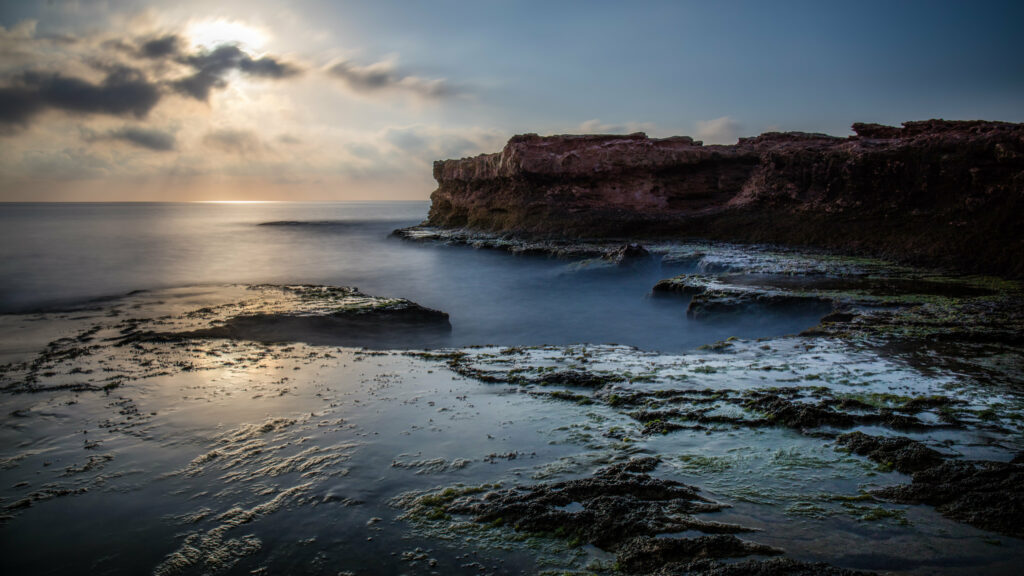 Dramatic coastal landscape with rugged rocks smooth sea waves and soft sunlight glowing blue tones Wallpaper