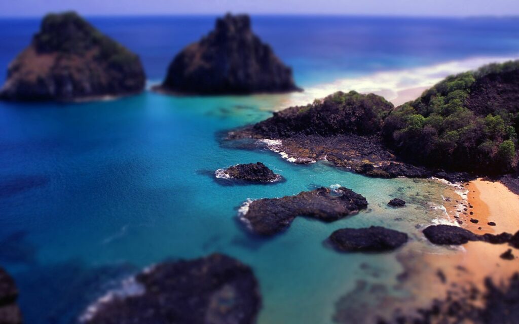 Tilt-shift coastal wallpaper with rugged rocks turquoise bay lush greenery and sandy shores view