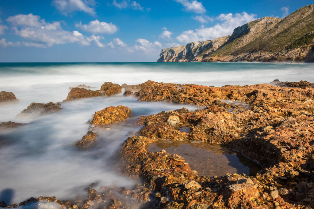 Coastal reef with rugged rocks smooth misty water serene blue sea and dramatic mountains wallpaper
