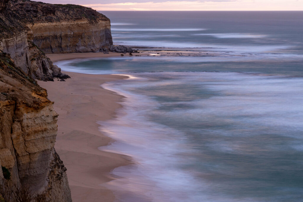 Sunset coastal wallpaper with rugged rocks smooth sandy shores gentle surf and pastel sky