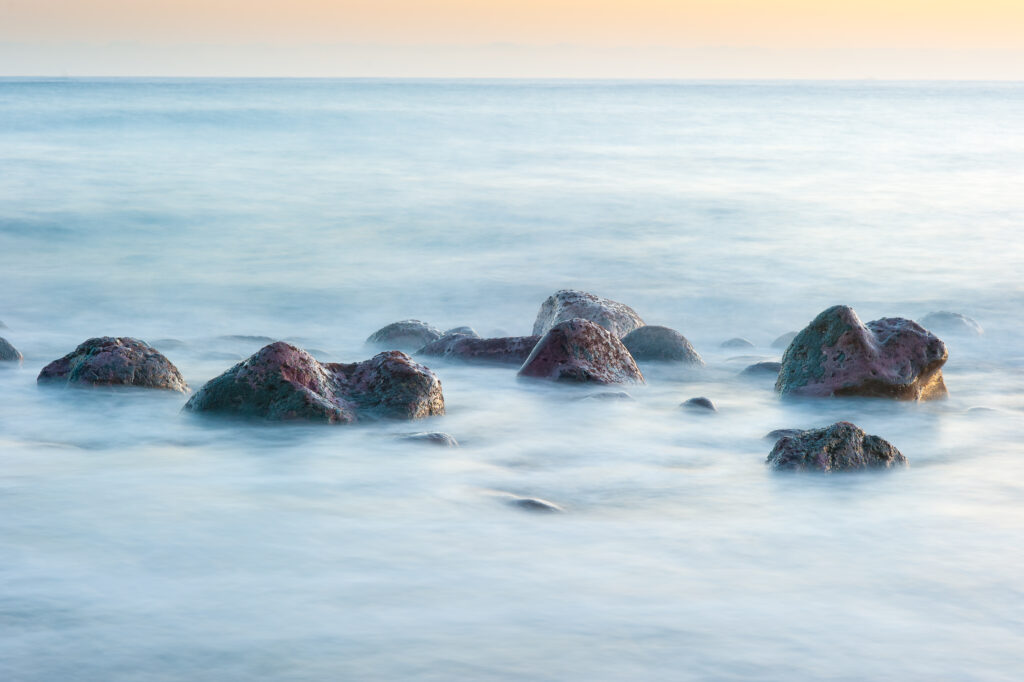 Soft pastel stones in calm sea with blurred waves long exposure serene nature wallpaper background