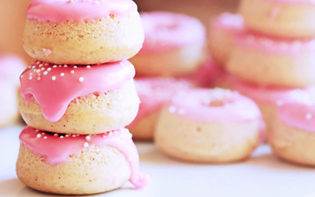 Stack of fluffy donuts with glossy pink icing and white sprinkles on dreamy soft background Wallpaper