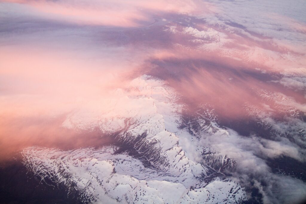 Aerial view of snow-capped mountains in pink light with wispy clouds serene wallpaper background