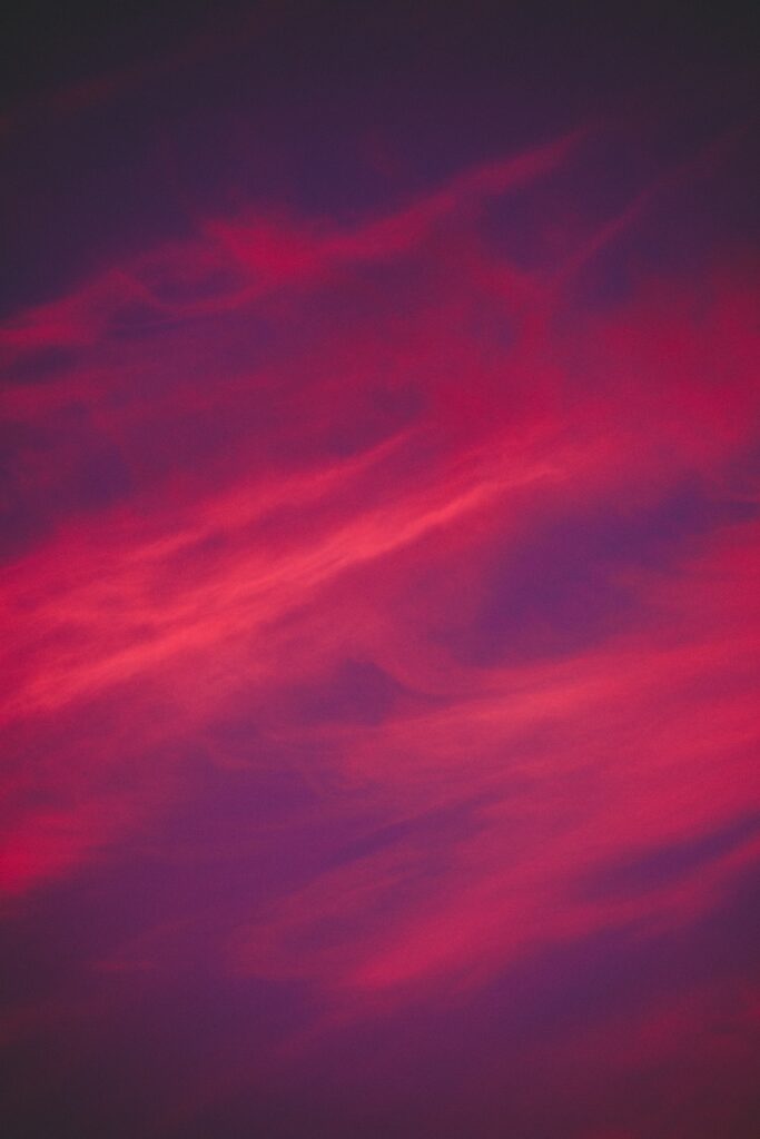 Abstract wallpaper with wispy porous clouds swirling in vibrant pink and deep purple sky