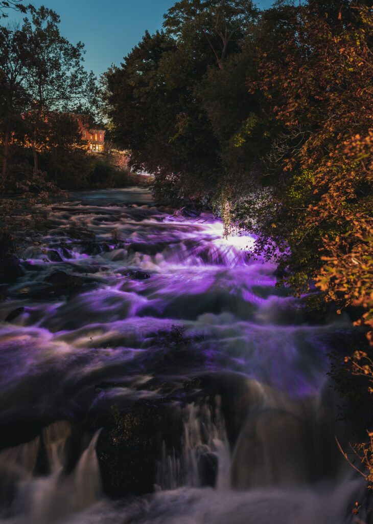 Vibrant river flowing over rocks with purple sunset glow lush trees and dramatic lighting wallpaper background