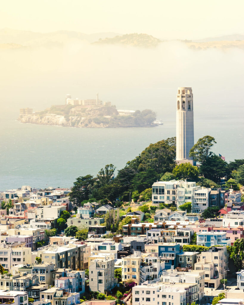 Coit Tower above colorful San Francisco homes with Alcatraz Island and misty bay waters view Wallpaper