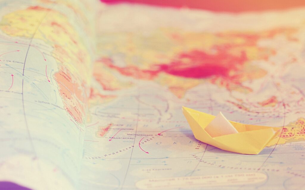 Vibrant Travel Wallpaper: Dreamy Yellow Paper Boat on World Map
