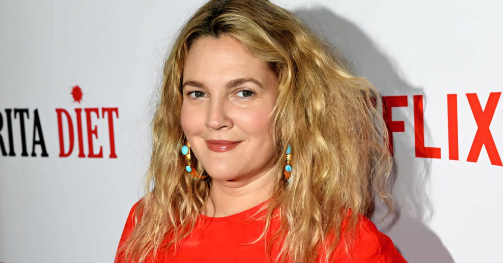 Drew Barrymore in bright red top with wavy blonde hair smiling at Netflix event vibrant wallpaper
