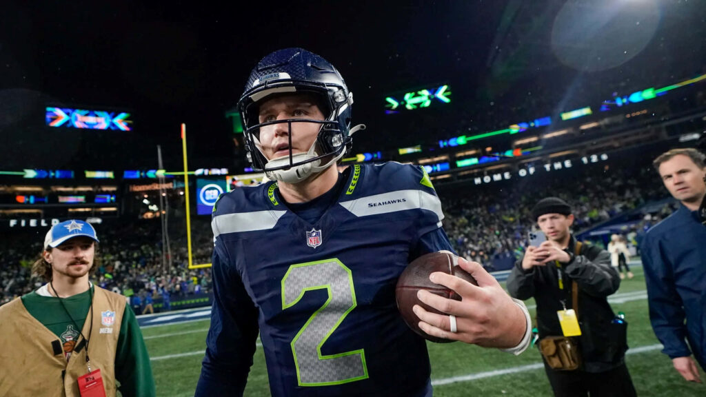 Drew Lock in Seahawks number 2 jersey steps off illuminated field clutching football game night Wallpaper