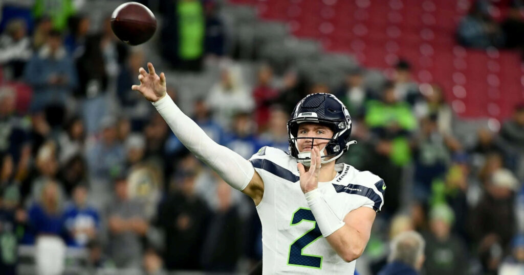 Drew Lock throwing football in Seattle Seahawks uniform during game with vibrant stadium crowd Wallpaper