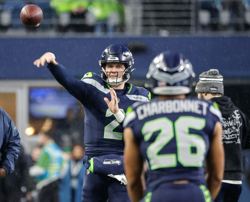Drew Lock throwing football with Zach Charbonnet in Seattle Seahawks uniforms vibrant stadium background Wallpaper