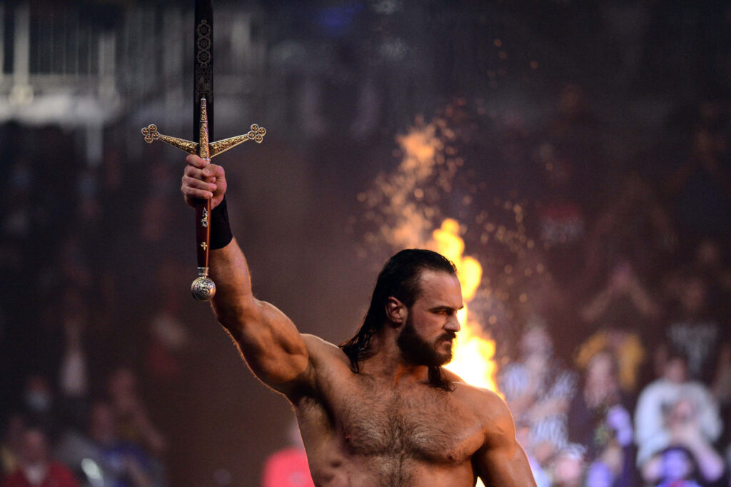 Drew McIntyre WWE Scottish Warrior raises sword with flames in arena intense dramatic lighting Wallpaper
