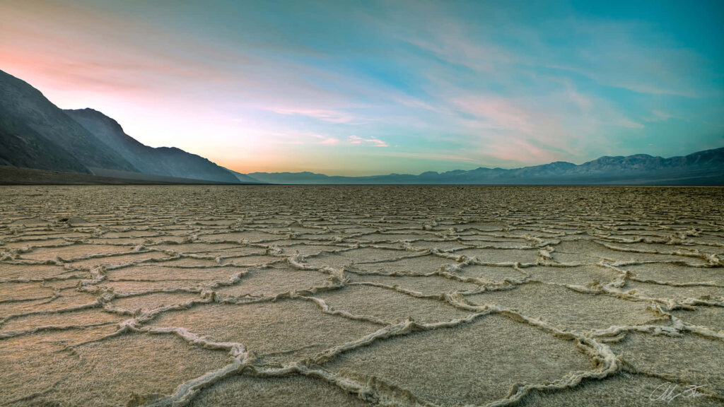 Dry cracked soil on deserted plain with distant mountains at sunrise showing drought effects Wallpaper