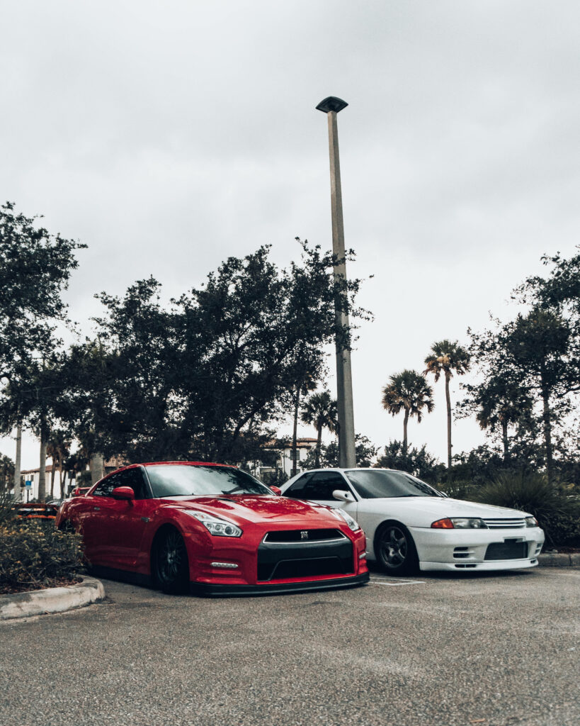 Two modified Nissan Skyline GTR R34 cars parked side by side with palm trees and cloudy sky background Wallpaper
