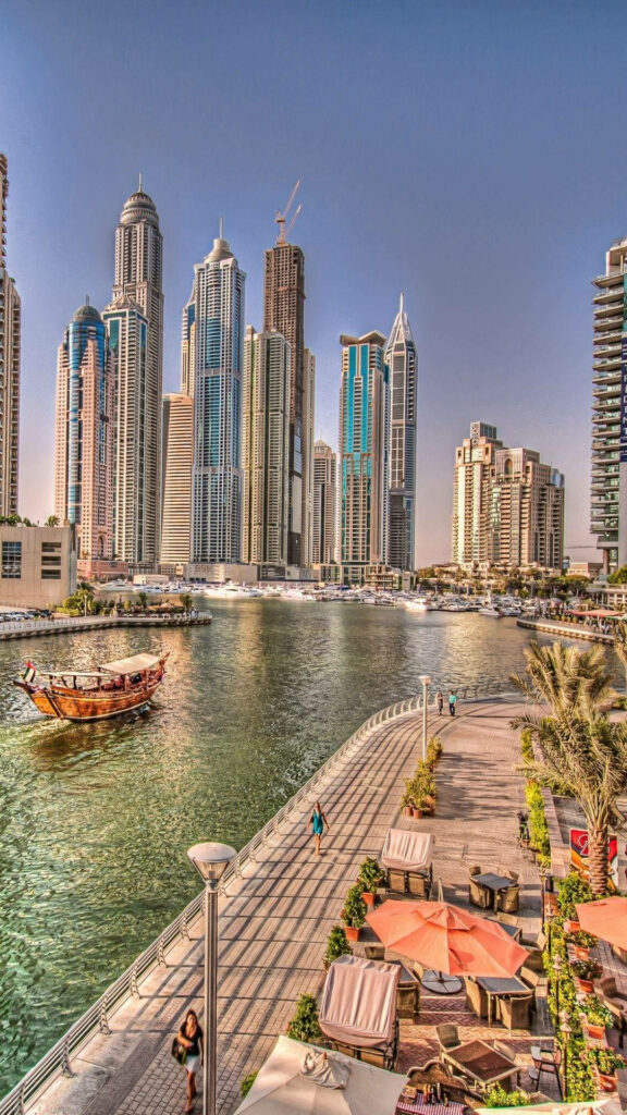 Dubai riverside wallpaper with modern skyscrapers wooden boat palm trees and serene waterfront view