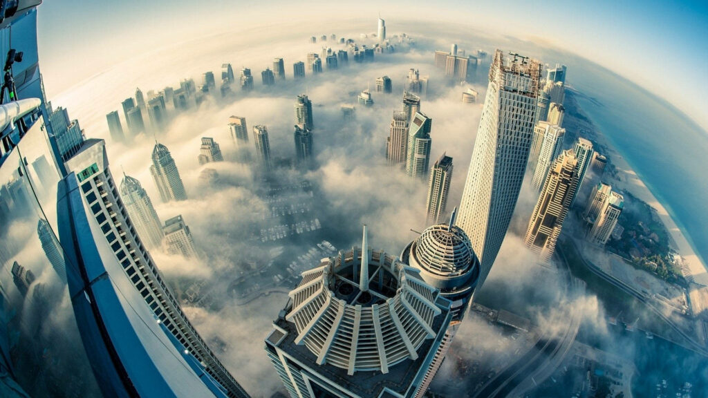 Aerial view of Dubai skyscrapers emerging through clouds in soft blue morning light wallpaper