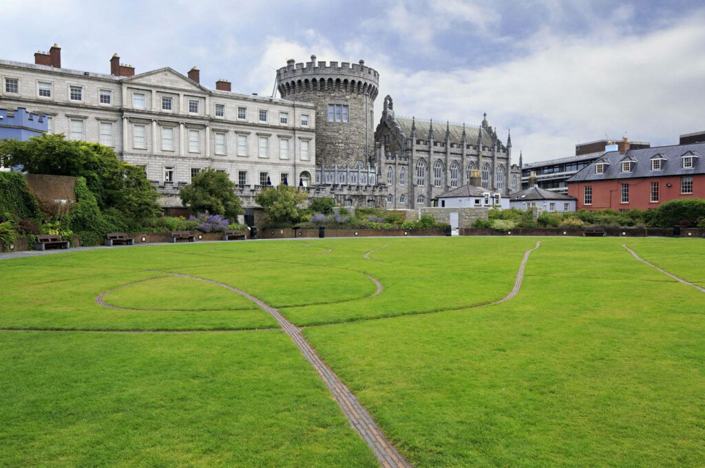 Historic Dublin Castle stone facade with lush green field and partly cloudy sky wallpaper background