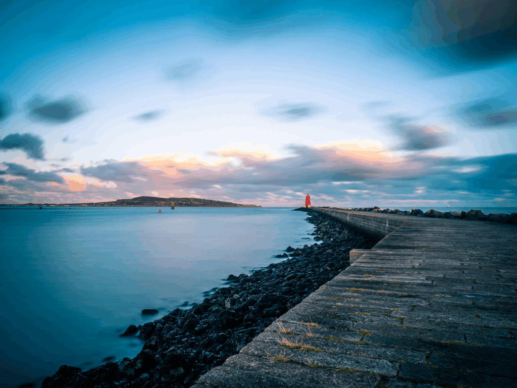 Dublin pier leading to red lighthouse over calm blue sea under soft cloudy sky wallpaper background