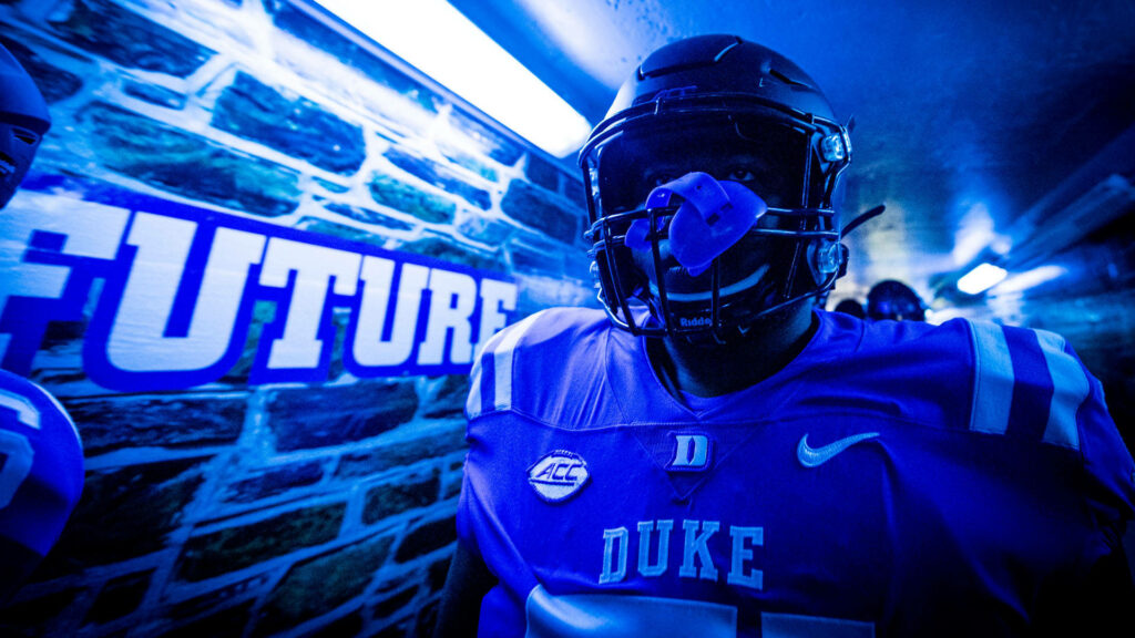 Duke Blue Devils football player in blue white gear stands in tunnel with blue lights and stone walls Wallpaper