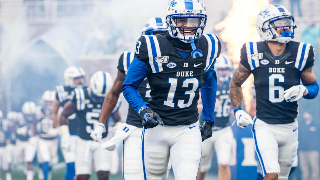 Duke Blue Devils football team charging onto field with smoke flames intense game day energy Wallpaper