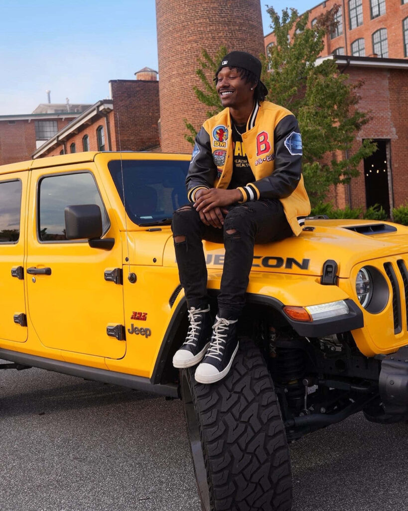 Duke Dennis confident in letterman jacket on yellow Jeep Rubicon urban brick background wallpaper