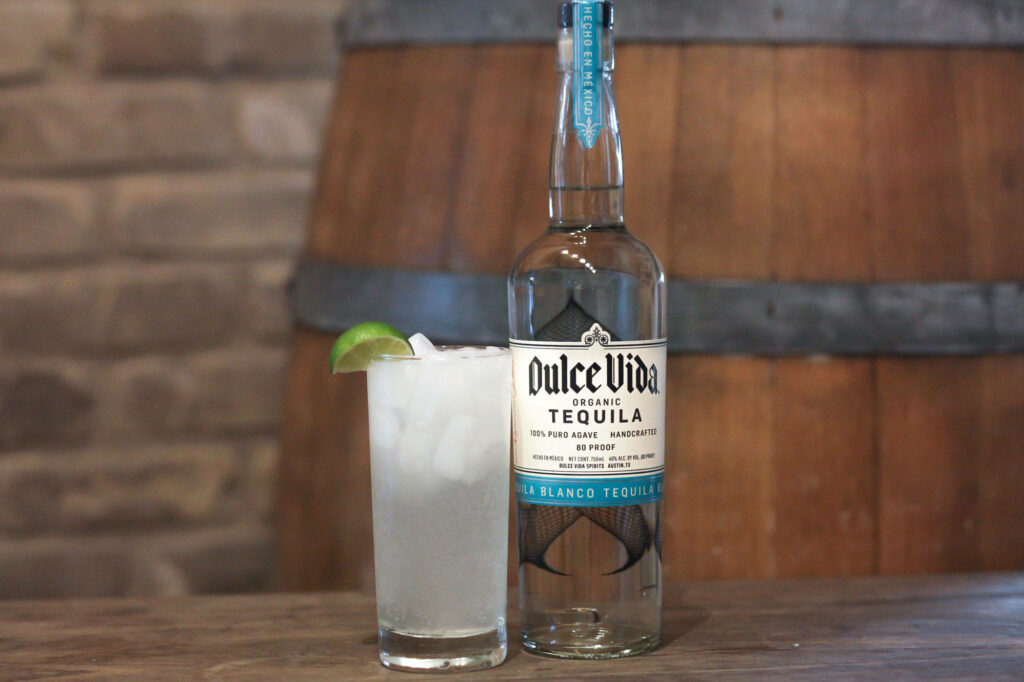 Dulce Vida organic tequila bottle and iced lime cocktail on rustic wooden barrel background Wallpaper